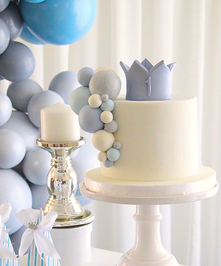 Bolo branco decorado com esferas azuis e topo de coroa para festa de primeiro aniversário com tema azul.