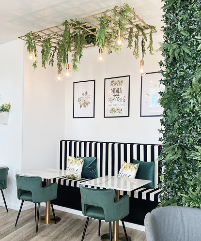 Interior elegante da confeitaria Limão Papoila com decoração moderna, mesas de mármore, cadeiras verdes e sofás listrados com almofadas decorativas.